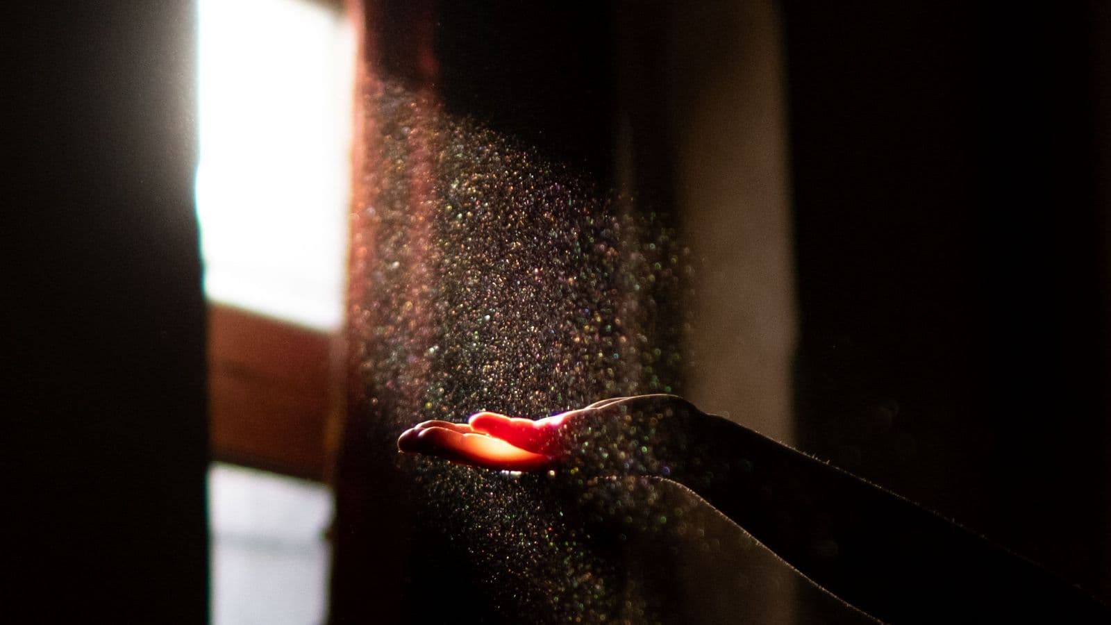 A hand running a fingertip through dust in a bright sunbeam, a reminder of the indoor dust that holds dust mite allergen.