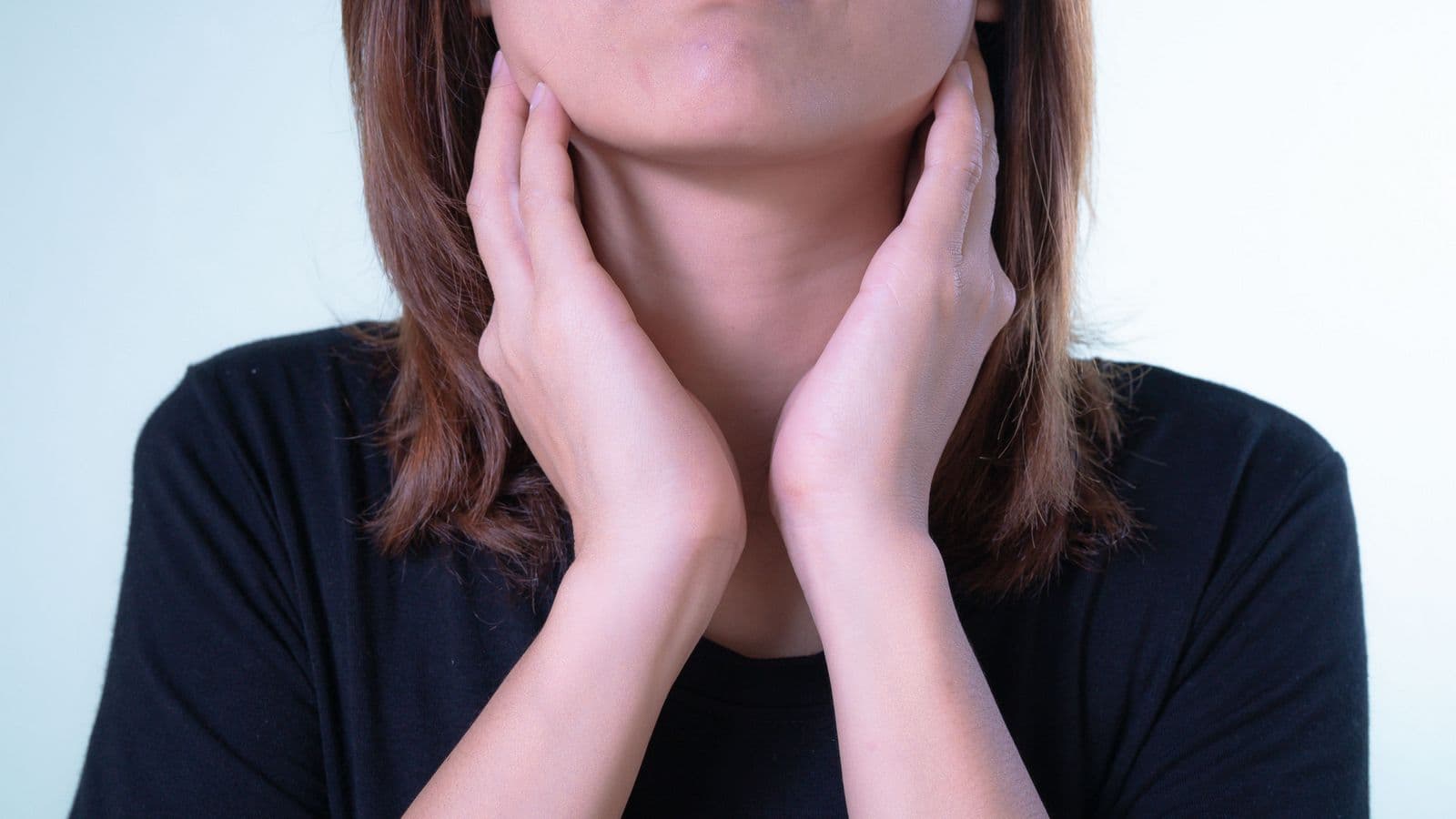 A person holding both hands to the sides of their throat, a common sign of a sore throat